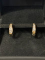 A pair of gold huggie hoop earrings with pavé-set clear stones, displayed inside a black velvet jewelry box.