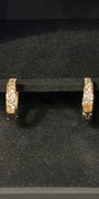 A pair of gold huggie hoop earrings with pavé-set clear stones, displayed inside a black velvet jewelry box.