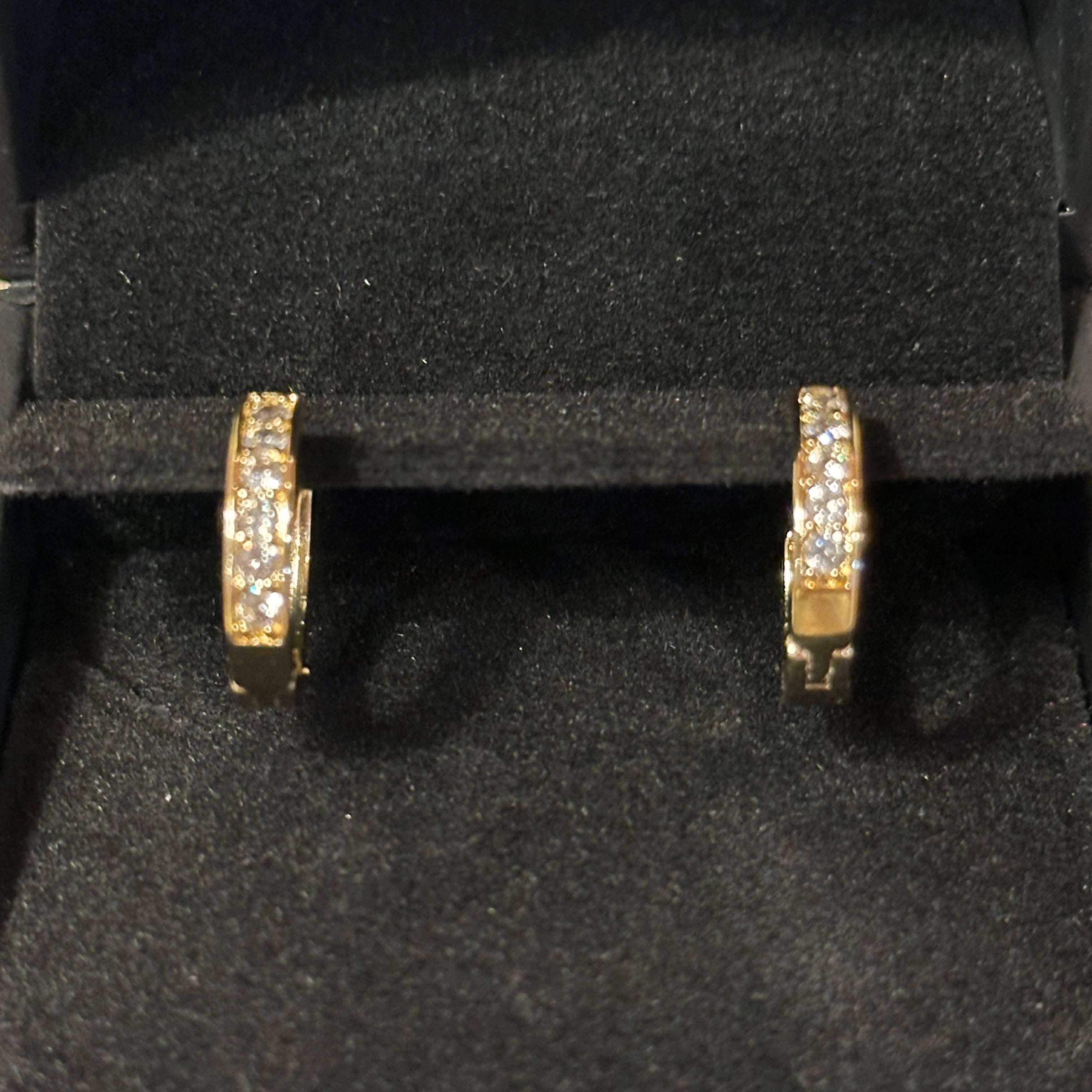 A pair of gold huggie hoop earrings with pavé-set clear stones, displayed inside a black velvet jewelry box.