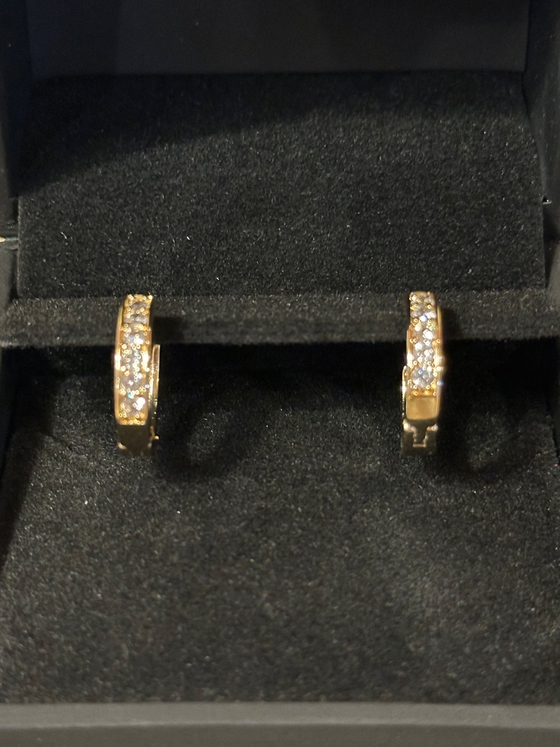 A pair of gold huggie hoop earrings with pavé-set clear stones, displayed inside a black velvet jewelry box.