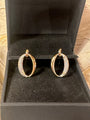 A pair of gold hoop earrings with pavé-set clear stones, displayed inside an open black jewelry box.