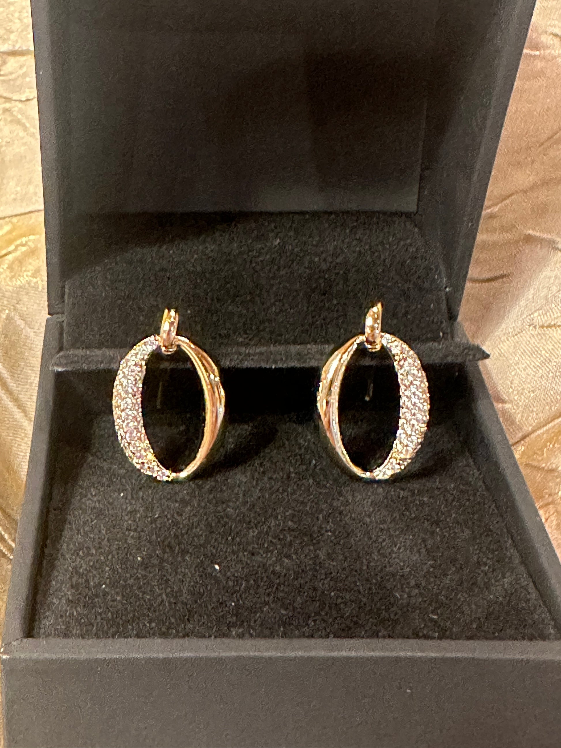 A pair of gold hoop earrings with pavé-set clear stones, displayed inside an open black jewelry box.