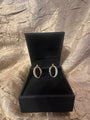 A pair of gold hoop earrings with pavé-set clear stones, displayed inside an open black jewelry box on a textured metallic gold fabric background.