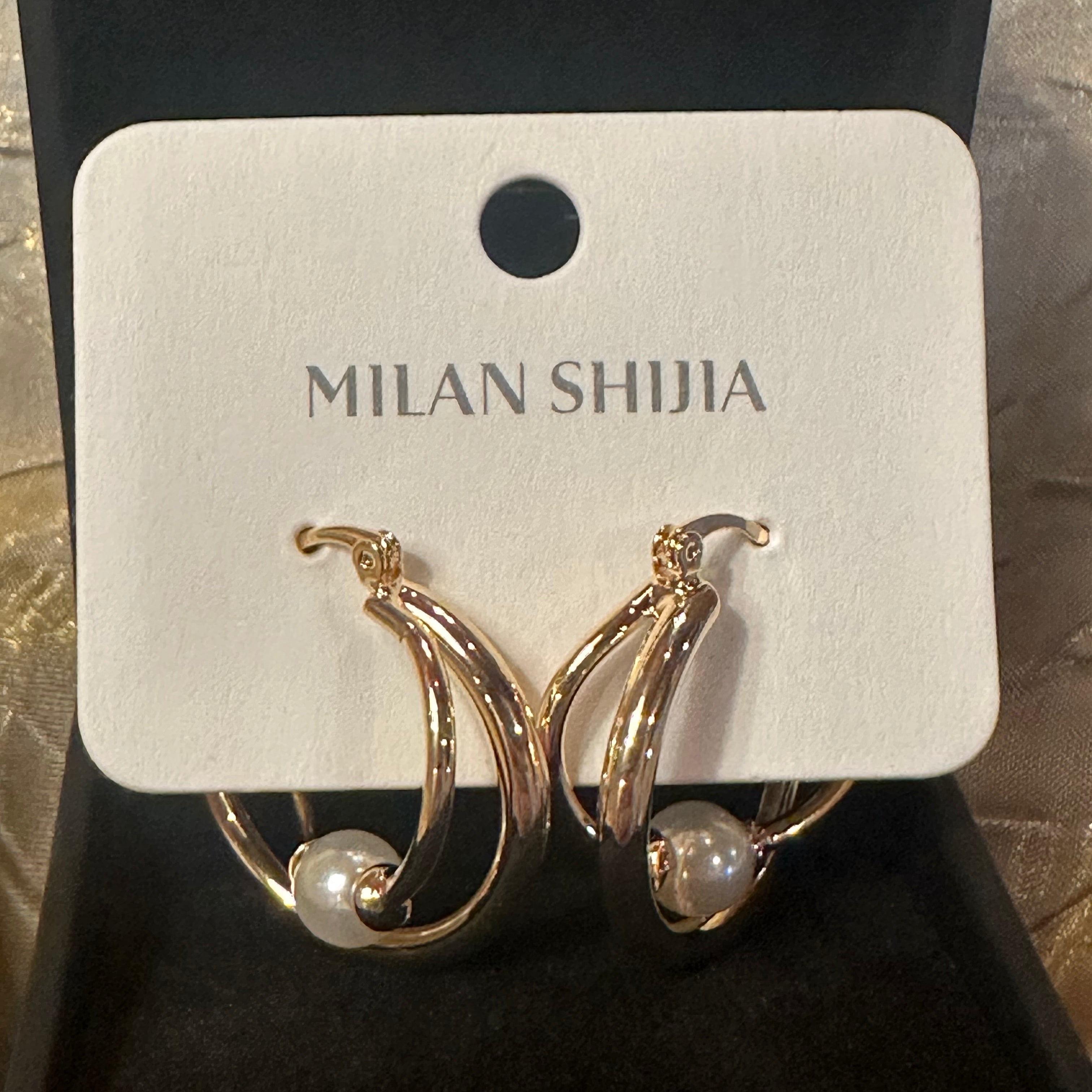 Gold crescent hoop earrings with a small white pearl, displayed on a white card labeled 'MILAN SHIJIA' inside a black jewelry box.