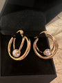 A pair of gold hoop earrings with a central white pearl, displayed inside a black jewelry box.
