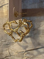 Gold-toned statement earrings with a sculptural, organic looped shape, shown hanging from a white display card against a textured silver fabric background.