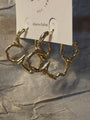 Gold hoop earrings with a textured, organic branch-like design, displayed on a white retail card labeled 'Atlanta-Dallas' against a shimmering silver fabric background.