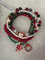 A set of five Christmas-themed beaded stretch bracelets on a white textured background. The bracelets feature red, green, and white beads, pearl-like white beads, gold-tone spacer rings, and charms including a Santa Claus figure, a red stocking, and a red and green wreath.