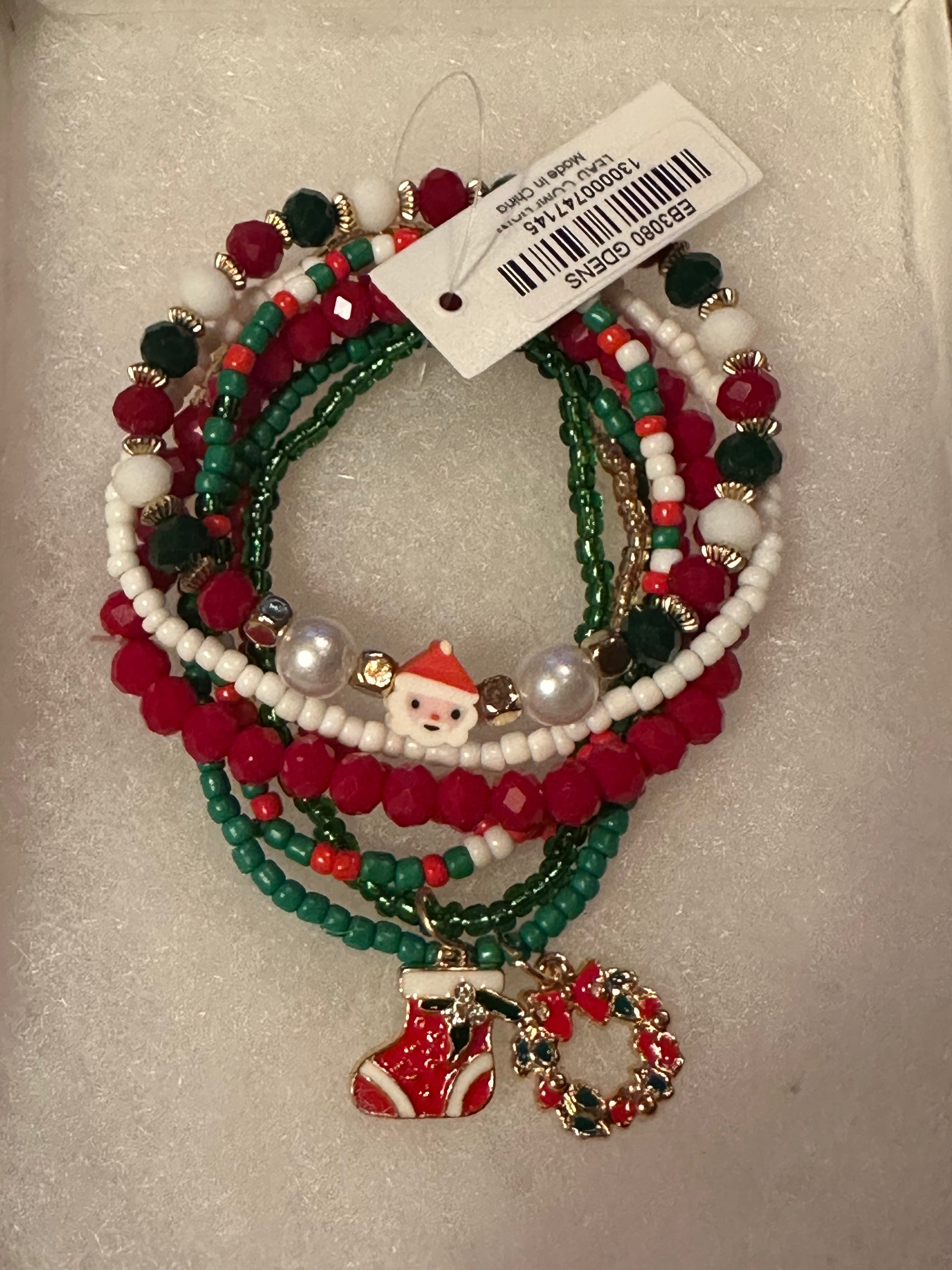 A set of Christmas-themed beaded bracelets with red, green, and white beads, pearl accents, a Santa Claus charm, and a red-and-green wreath charm, displayed on a white textured background with a product tag attached.