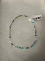A beaded stretch bracelet made of small translucent blue, green, and white beads with a few metallic silver beads, shown on a white textured background with a white product tag attached.