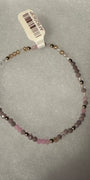 A beaded stretch bracelet with faceted pink, lavender, and metallic gold beads, shown with a white product tag on a textured gray background.