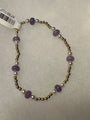 A beaded stretch bracelet featuring purple amethyst beads, white pearl-like beads, and metallic gold-toned spacer beads, shown on a textured light gray background with a white product tag attached.