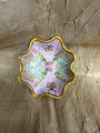 A scalloped ceramic dish with a gold rim, featuring a pastel pink and green abstract painted pattern with butterfly motifs, set against a textured gold background.