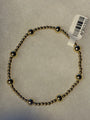 A beaded bracelet made of small metallic gold-toned beads with alternating polished silver-toned dome accents, shown on a textured white background with a white product tag attached.