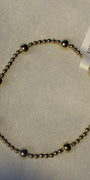 A beaded bracelet made of small metallic gold-toned beads with alternating polished silver-toned dome accents, shown on a textured white background with a white product tag attached.