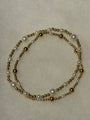 A double-strand beaded necklace featuring white faux pearls and polished gold-tone metal beads, arranged in a loose circle on a textured off-white background.