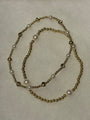 A beaded necklace featuring metallic gold-toned round beads and white faux-pearl accents, arranged in a loose loop on a textured off-white background.
