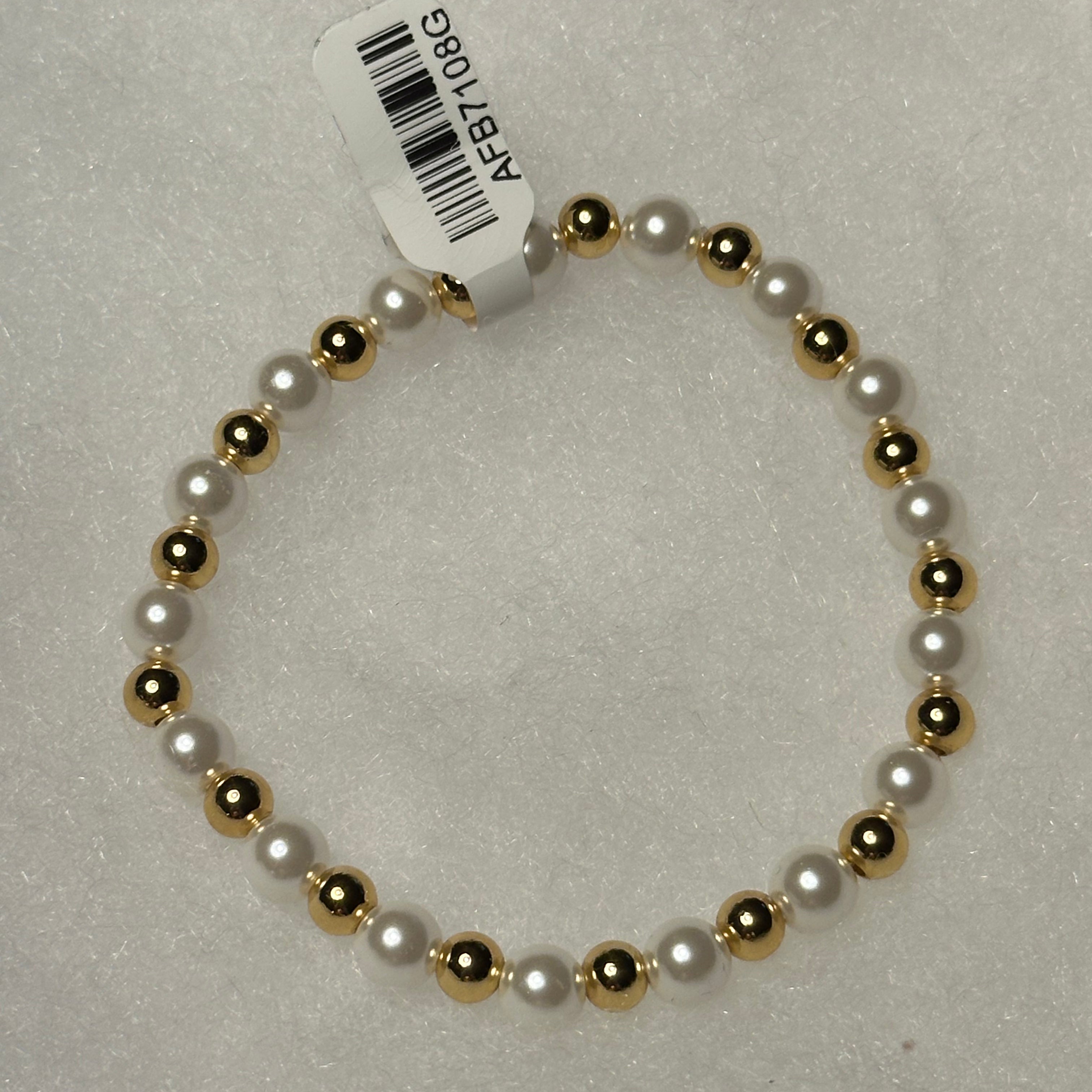 A beaded stretch bracelet featuring alternating white faux pearls and polished gold-toned beads, with a white paper tag attached.