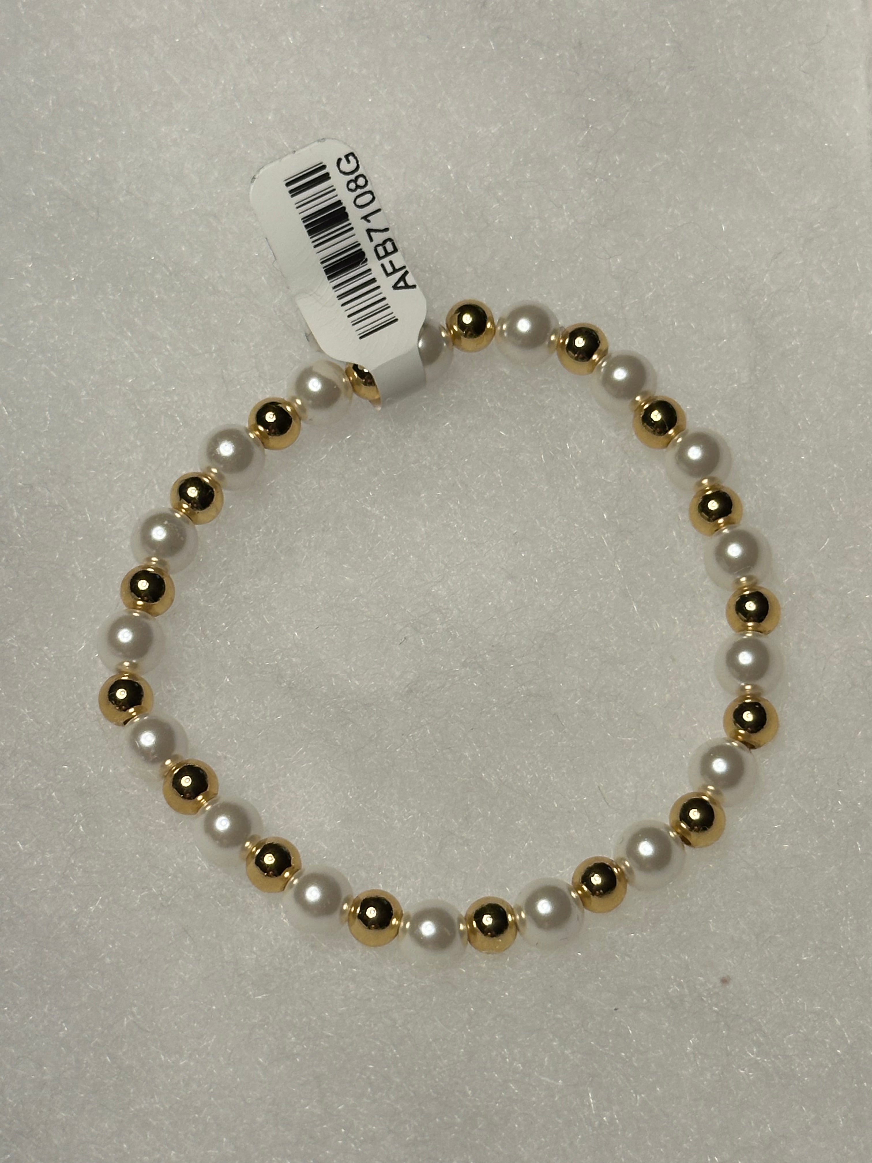 A beaded stretch bracelet featuring alternating white faux pearls and polished gold-toned beads, with a white paper tag attached.