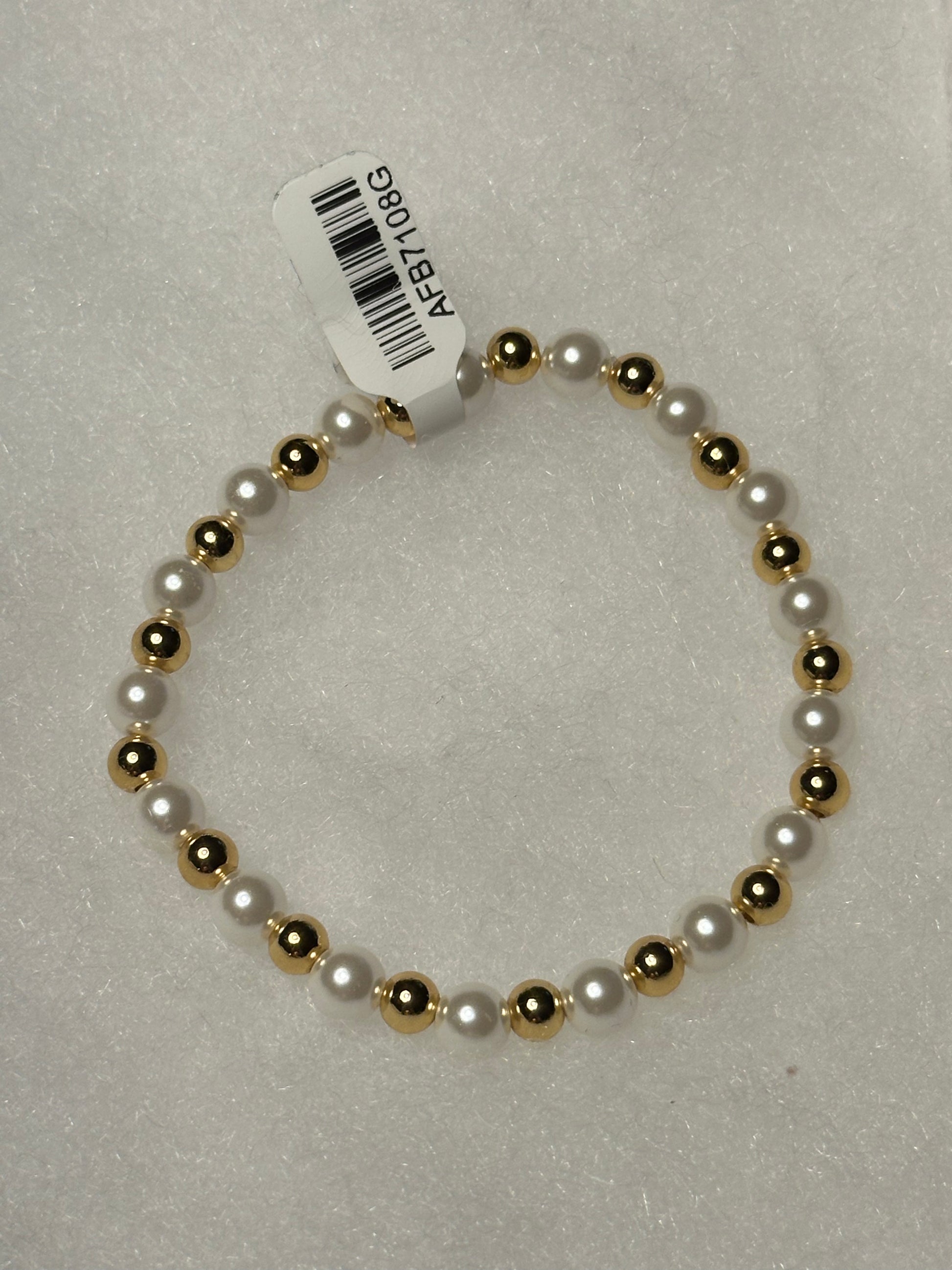 A beaded stretch bracelet featuring alternating white faux pearls and polished gold-toned beads, with a white paper tag attached.