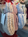 Stack of fluffy blankets with Barefoot Dreams tags on a red surface