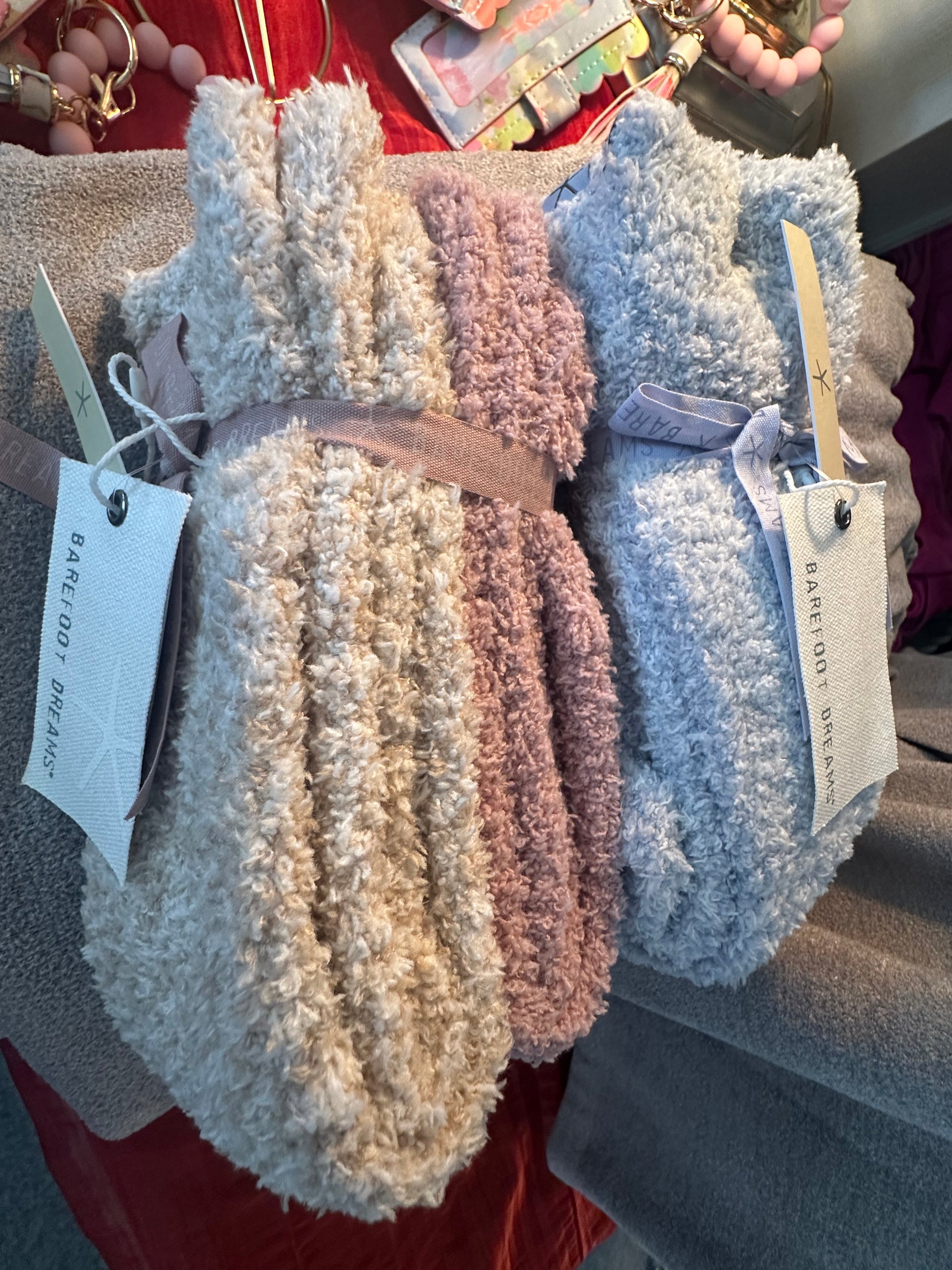 Stack of fluffy blankets with Barefoot Dreams tags on a red surface