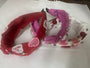 Three decorative headbands, one red . one white and one pink with heart and peaarl designs, on a white surface.