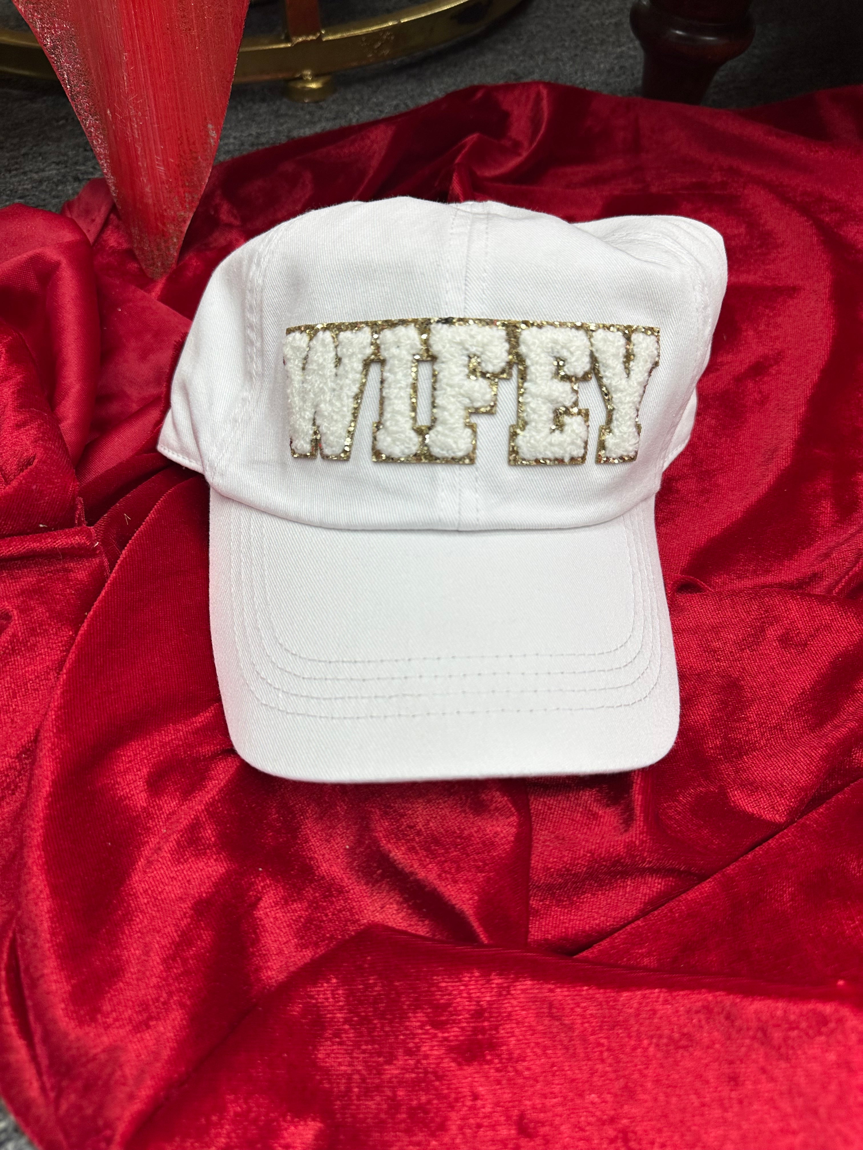 White cap with 'Wifey' embroidery on a red fabric background