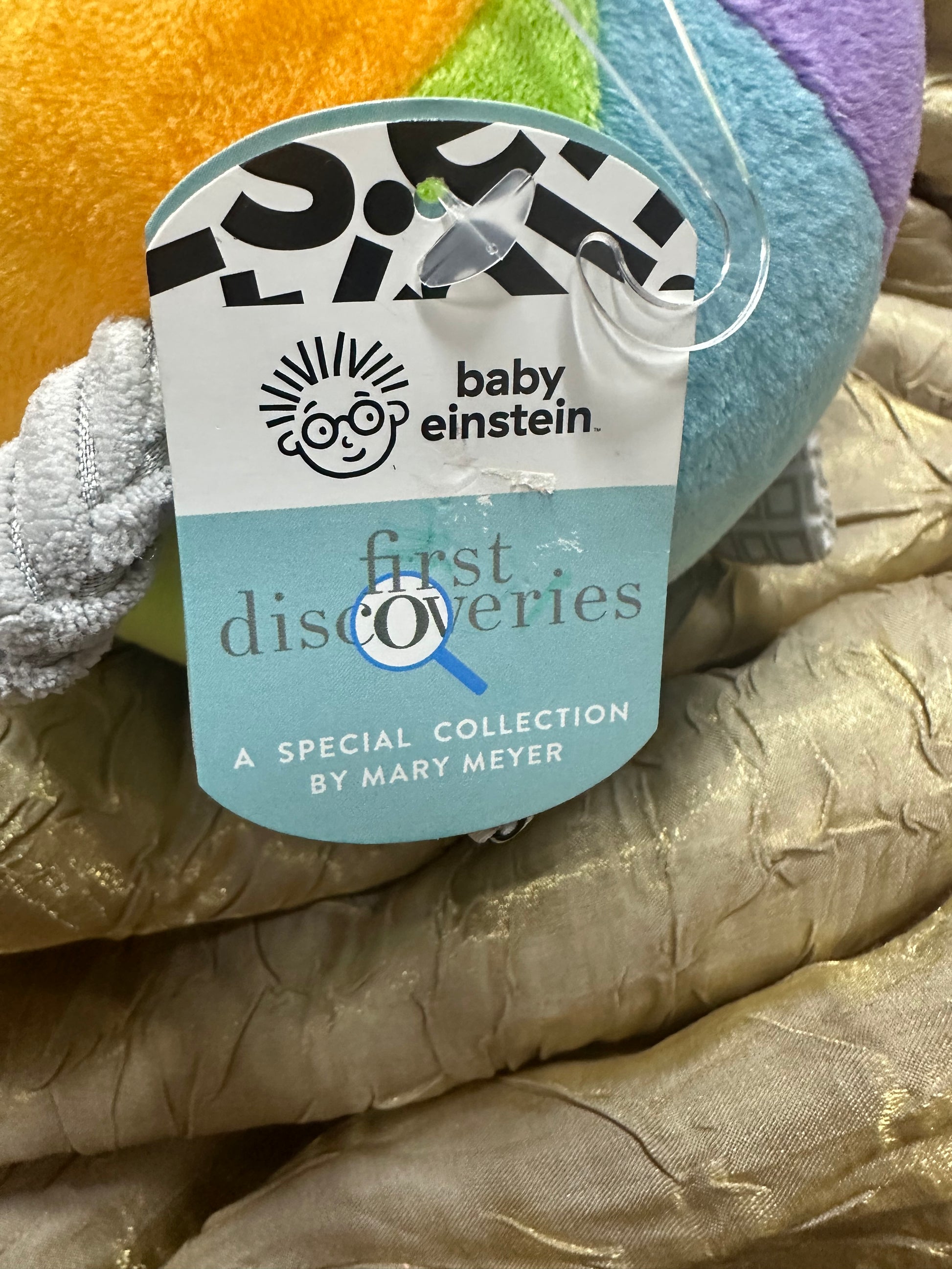 Close-up of a plush toy with a label featuring 'baby einstein' and 'first ferries' on a textured fabric background.
