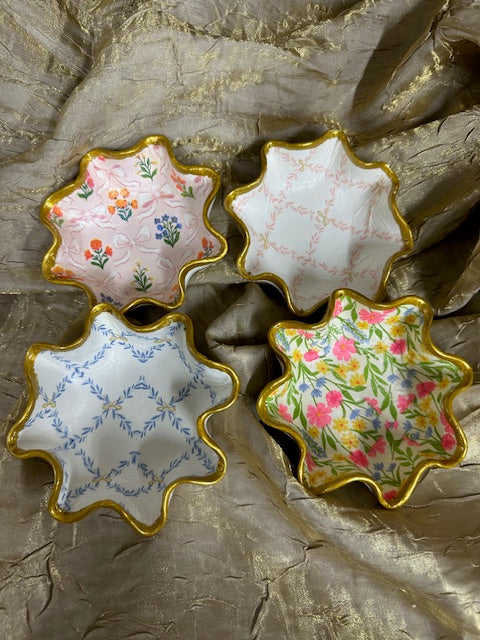 Four decorative star-shaped bowls with floral patterns on a textured surface