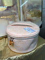 Round pink jewelry box with a gold zipper on a reflective surface