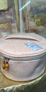 Round pink jewelry box with a gold zipper on a reflective surface