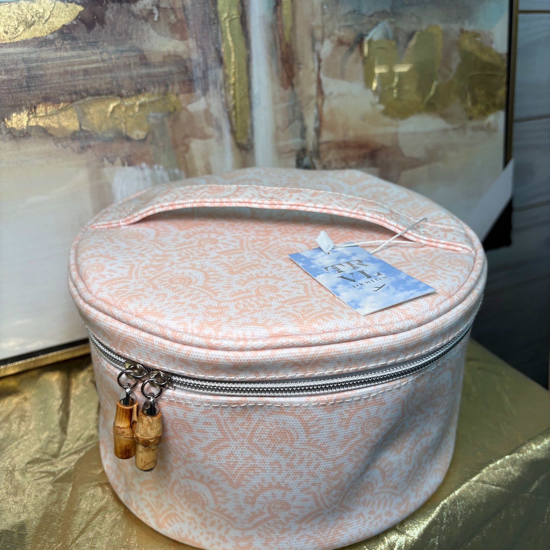 Round pink jewelry box with a gold zipper on a reflective surface
