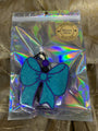 Blue glittery hair bow in a clear bag with a holographic pattern on a textured surface.