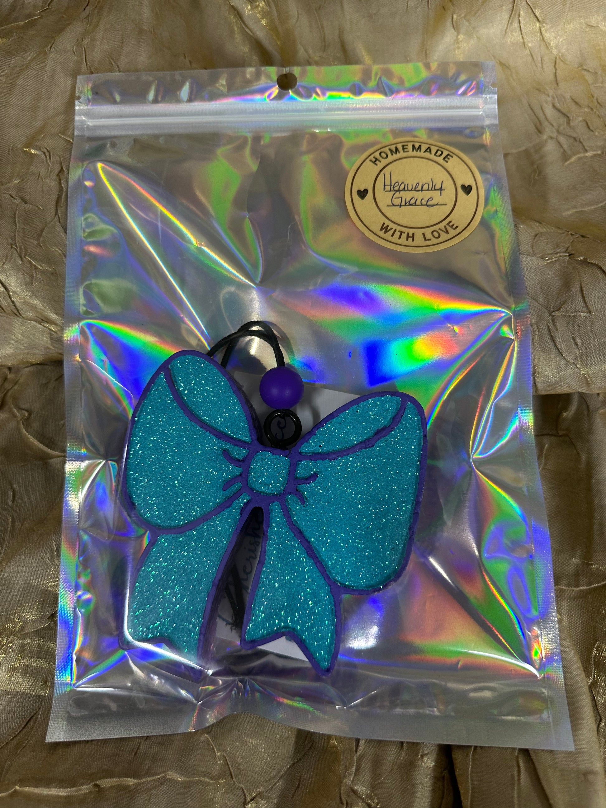 Blue glittery hair bow in a clear bag with a holographic pattern on a textured surface.