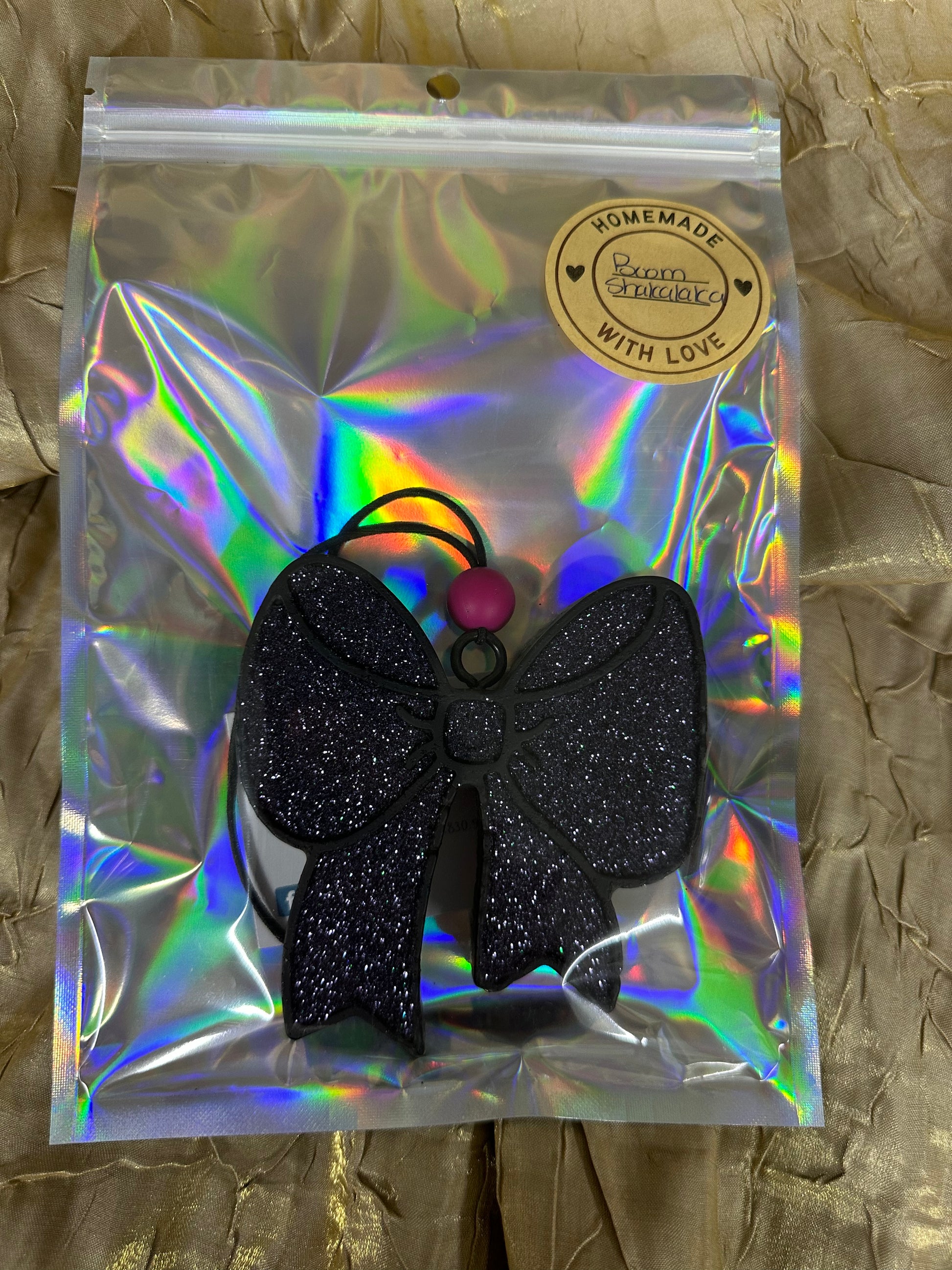 Black glittery bow hair tie in a reflective packaging on a textured brown background