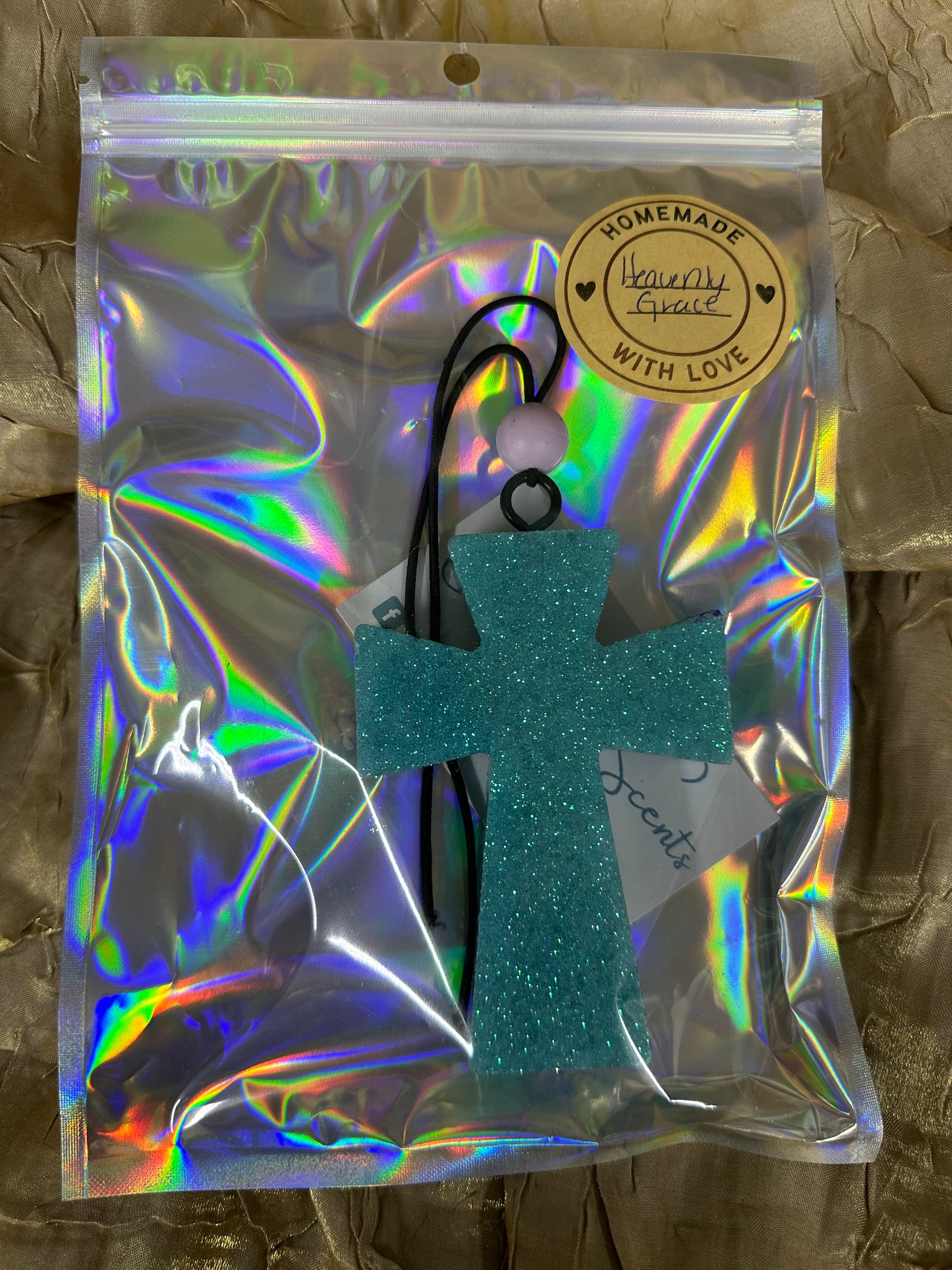 Turquoise glitter cross hair accessory in a reflective packaging bag on a textured brown background
