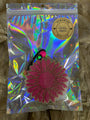 Holographic packaging with a pink flower-shaped object on a textured surface