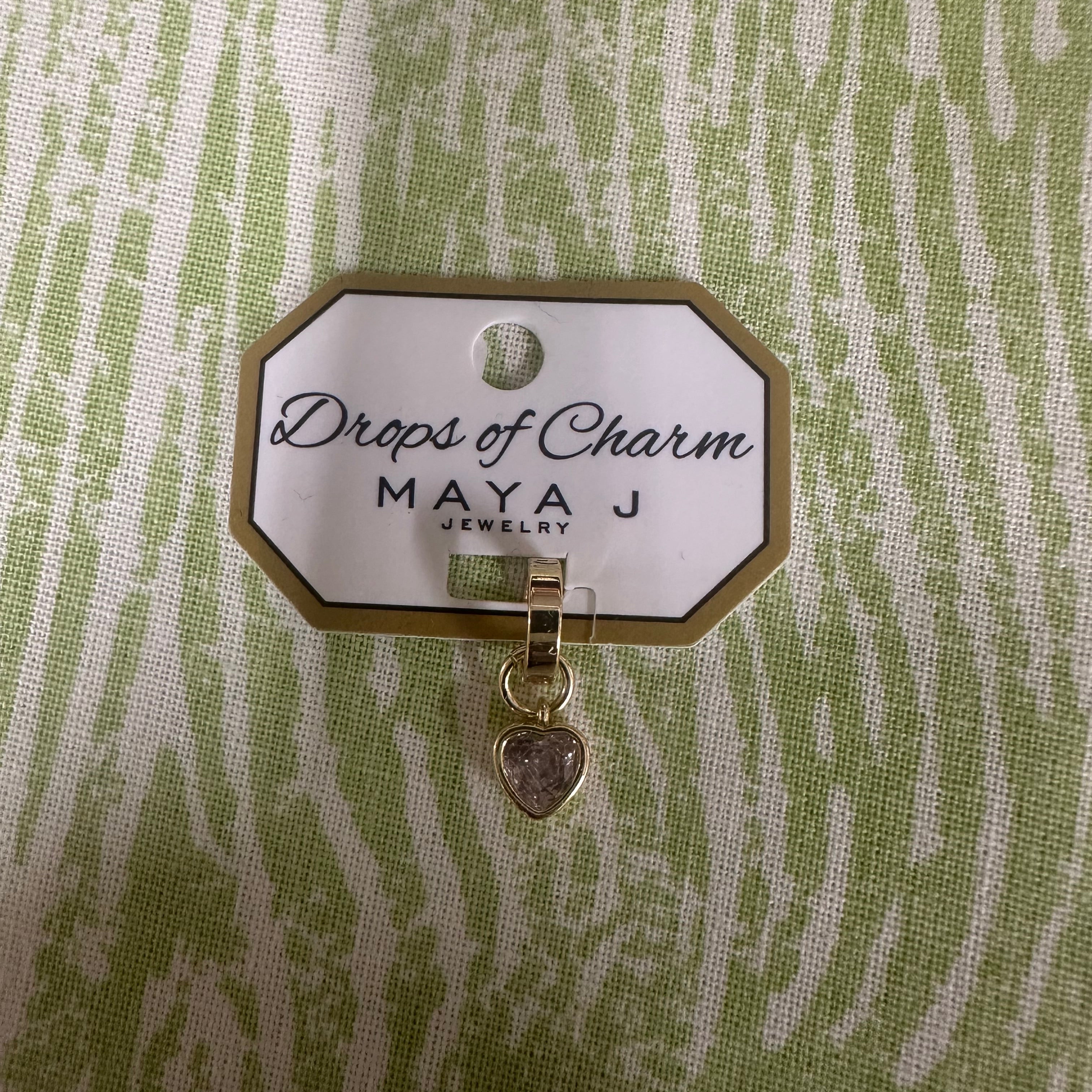 Yellow gold heart charm from Maya J called Drops of Charm on a green and white background