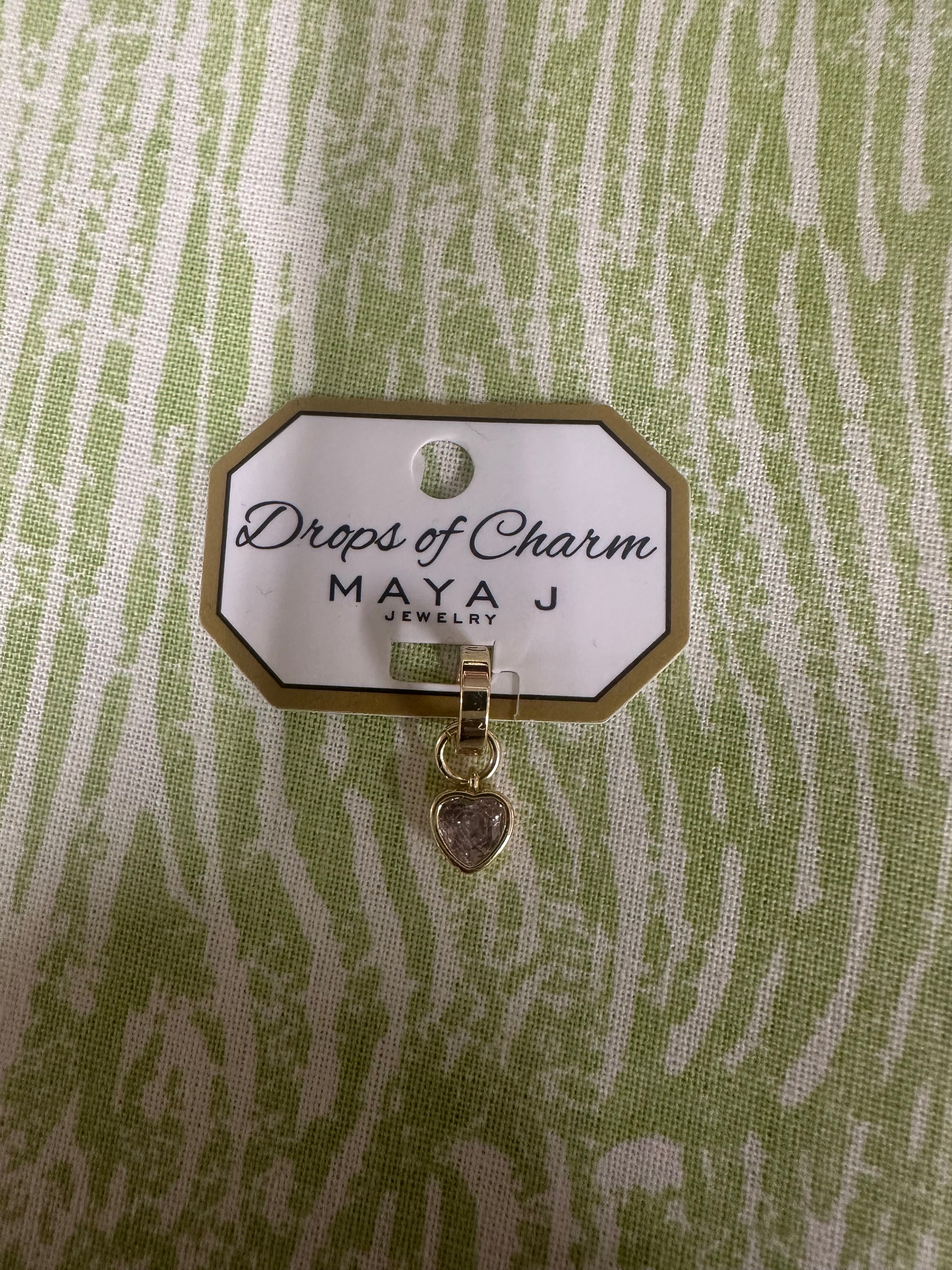 Yellow gold heart charm from Maya J called Drops of Charm on a green and white background