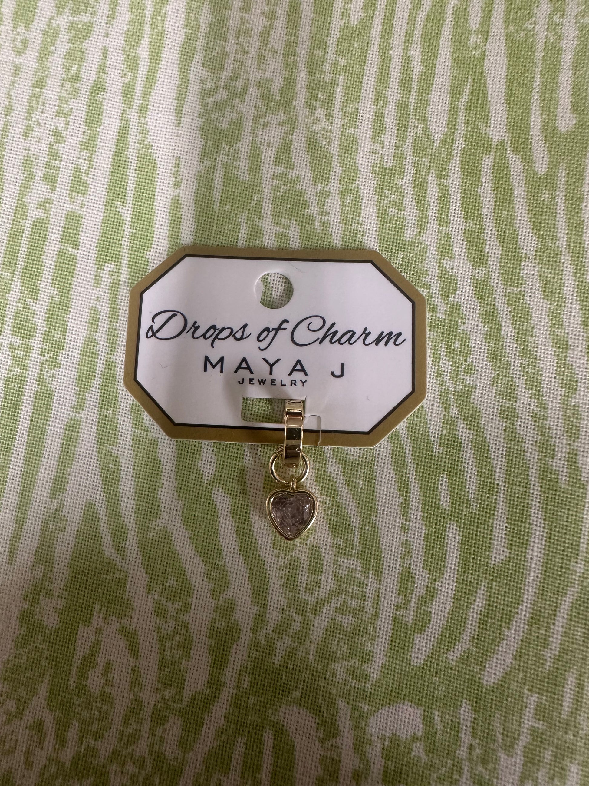 Yellow gold heart charm from Maya J called Drops of Charm on a green and white background