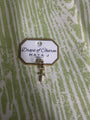 Yellow gold cross charm with 'Drops of Charm' label on a textured green background