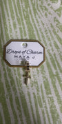 Yellow gold cross charm with 'Drops of Charm' label on a textured green background