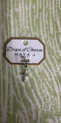 White gold charm with 'Drops of Charm' text on a textured green background