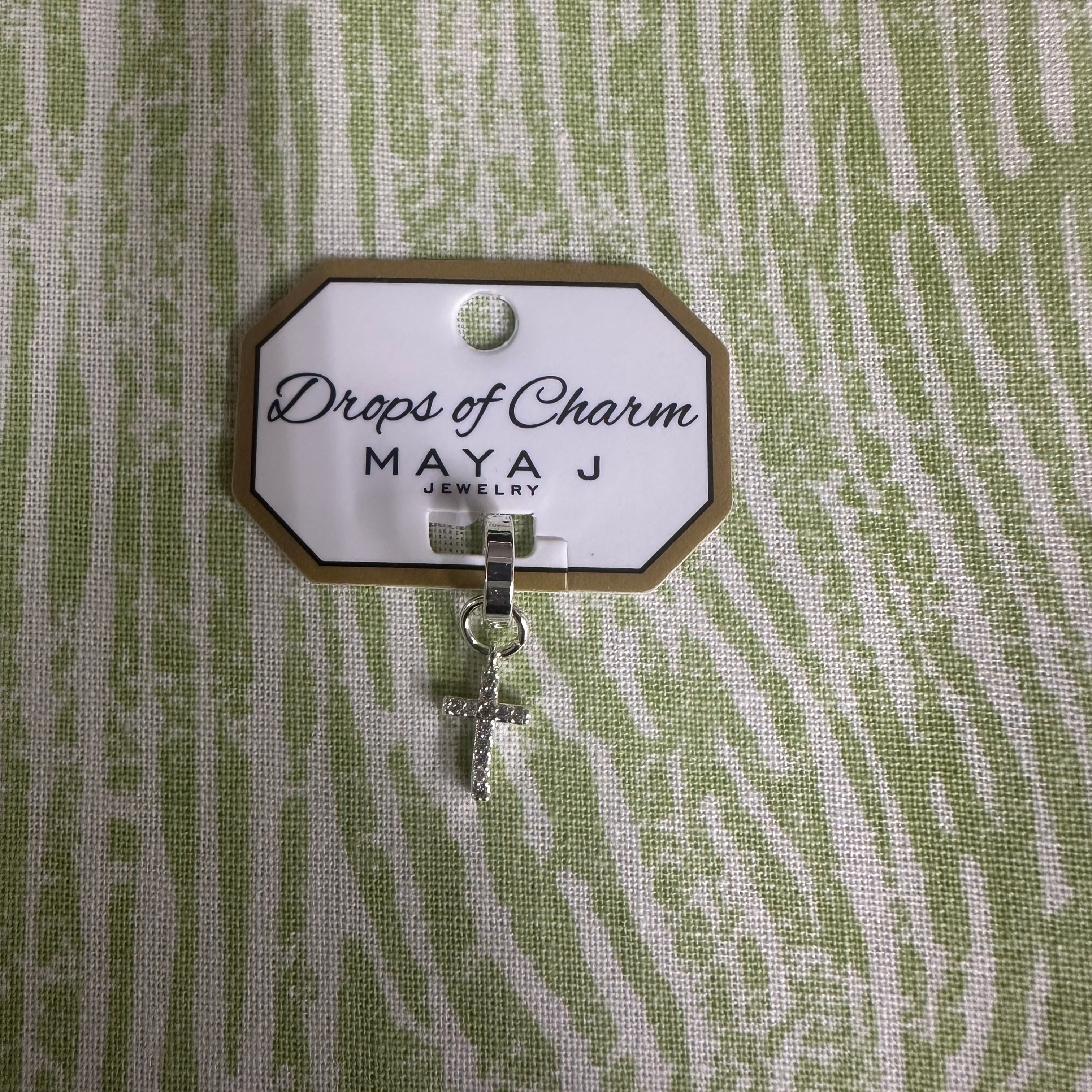 White gold charm with 'Drops of Charm' text on a textured green background