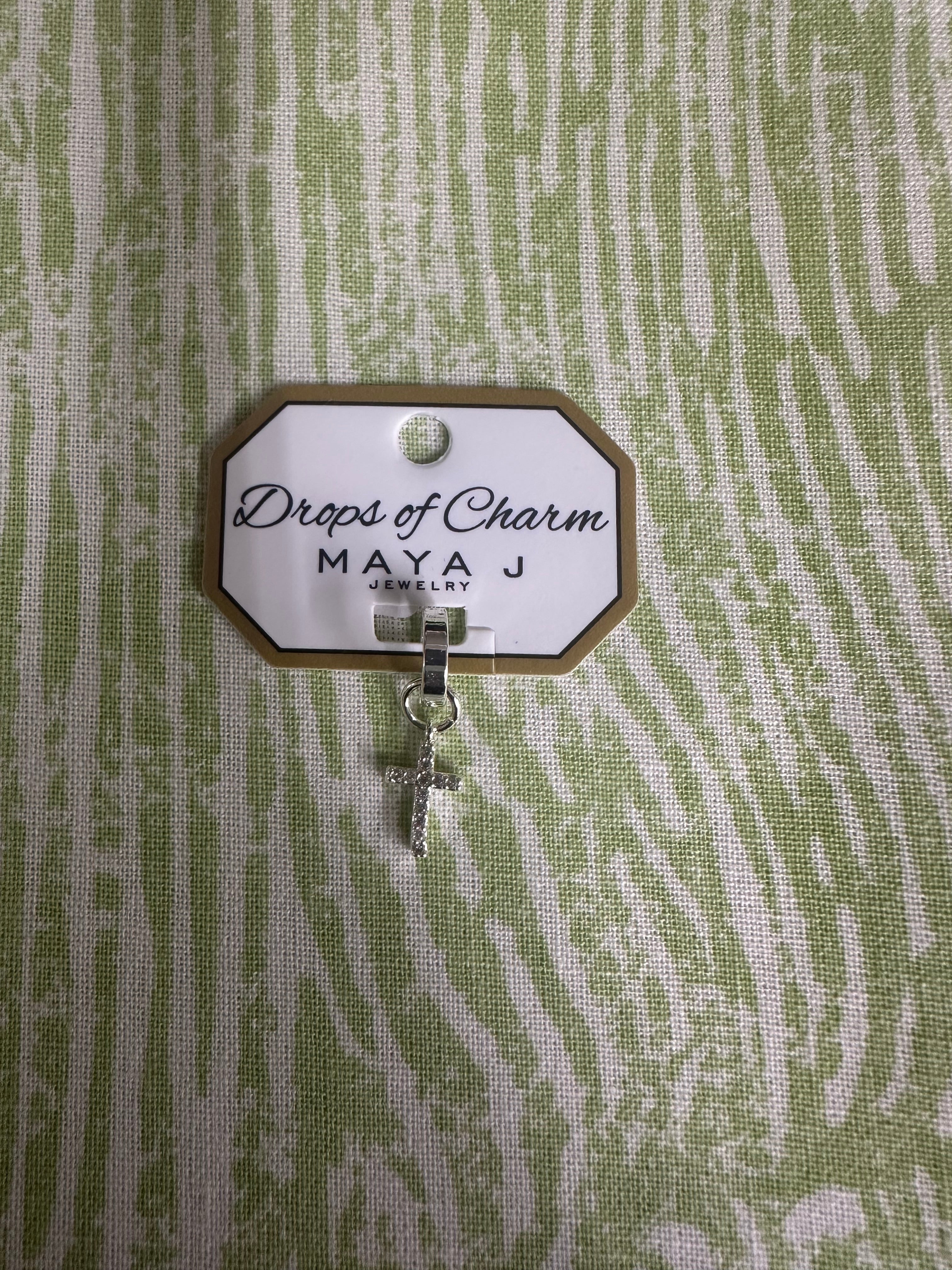 White gold charm with 'Drops of Charm' text on a textured green background