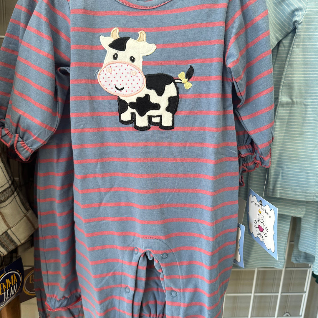 A baby long-sleeve footless romper with horizontal blue-gray and pink stripes, featuring a black-and-white cow applique on the chest, hanging on a wooden hanger on a retail display.