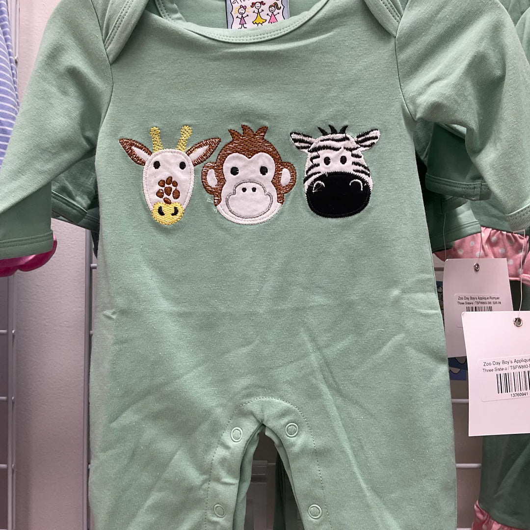 A mint green baby romper with three embroidered animal faces (giraffe, monkey, zebra) on the chest, hanging on a black hanger against a white wire display wall.