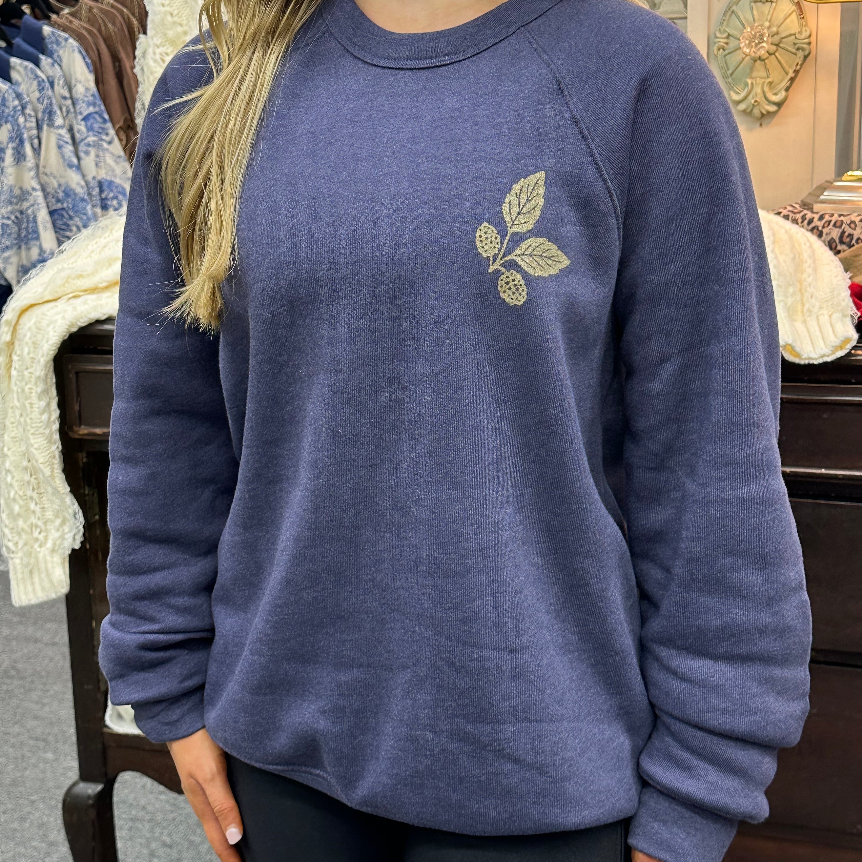 Person wearing a blue sweatshirt with a leaf design in a casual setting