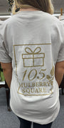 Person wearing a sand colored t-shirt with 105 Mulberry Square' printed on it, standing in a room.
